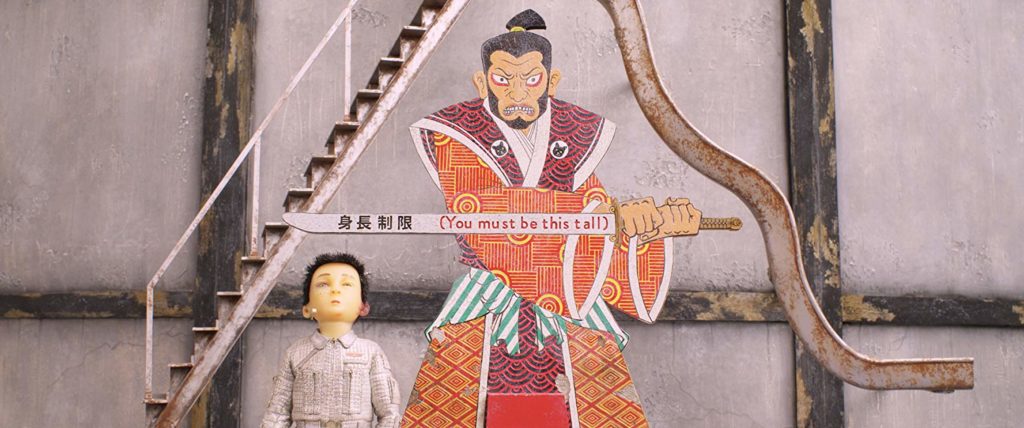 Atari ao lado de um poster. no poster, um samurai põe uma espada na horizontal. Na espada se lê "You must be this tall"