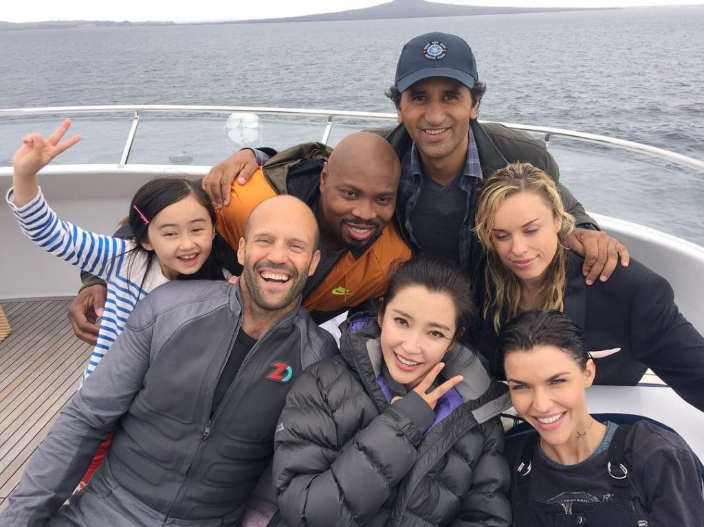 Jason Statham, Cliff Curtis, Bingbing Li, Page Kennedy, Jessica McNamee, Ruby Rose, e Shuya Sophia Cai em uma lancha, posando para foto. Cena de bastidores.