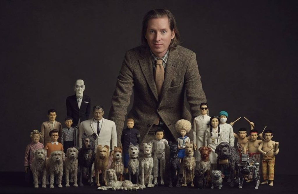 Ao fundo, Wes Anderson. À frente, os bonecos utilizados na animação Ilha dos Cachorros