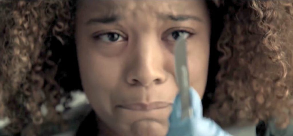 Chloe (Jaz Sinclair), em close, com olhar choroso, olhando para um bisturi (que está em primeiro plano)