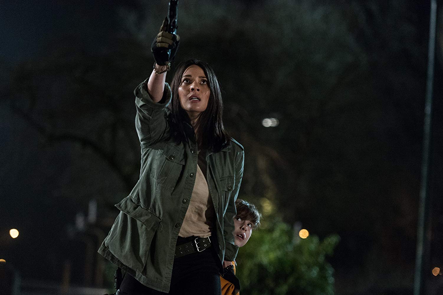 Dra. Bracket (Olivia Munn) apontando a arma para algo A frente dela (atrás da câmera), enquanto protege Rory (Jacob Tremblay), que está atrás dela, agarrando suas pernas