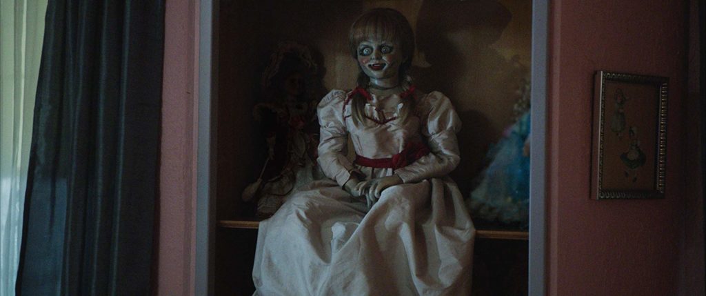 Boneca Annabelle sentada em uma prateleira com outras bonecas. Maratona de Sofá.