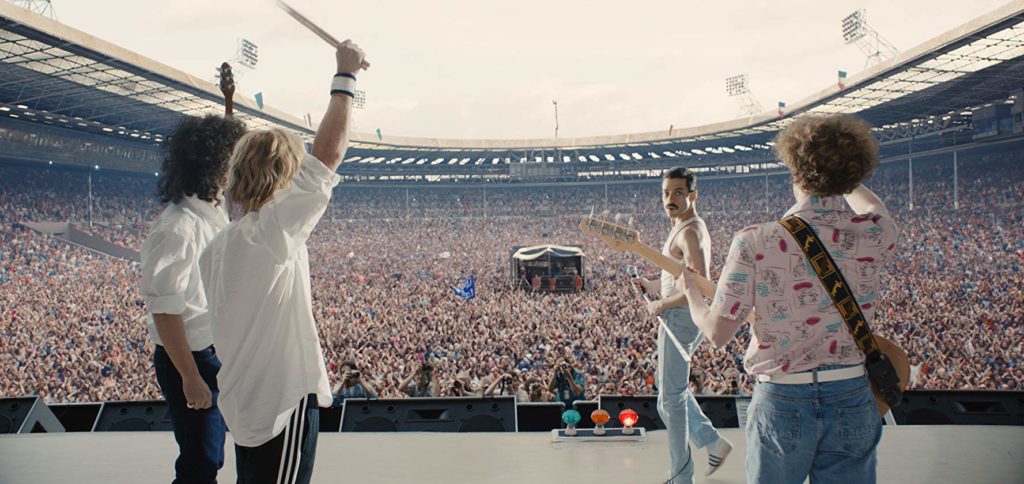 Visão do fundo do palco, mostrando a banda em primeiro plano (de costas), e mais ao fundo, a multidão lotando o estádio do Live Aid
