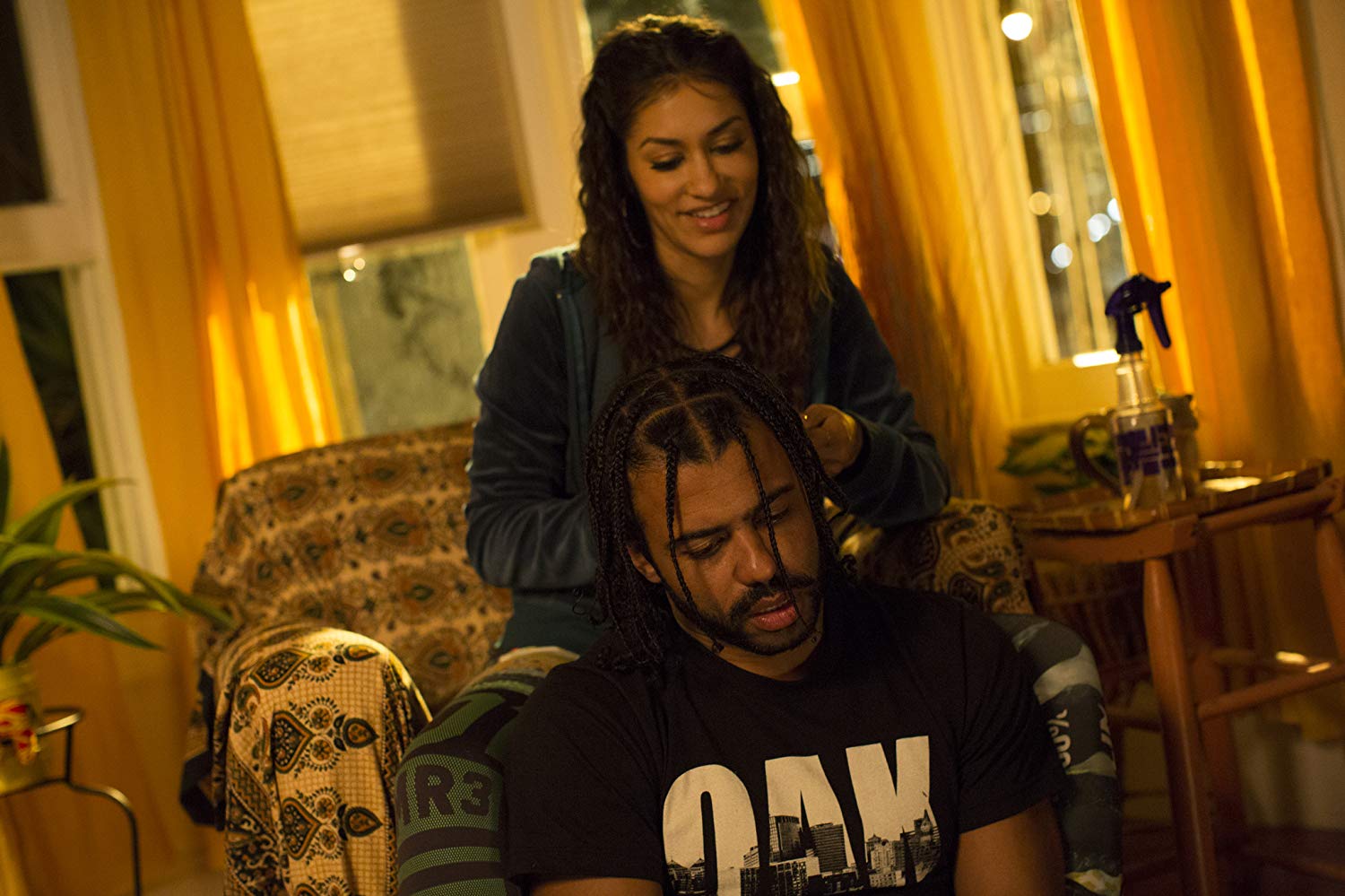 Val (Janina Gavankar) trançando o cabelo de Colin, que está sentado na sua frente