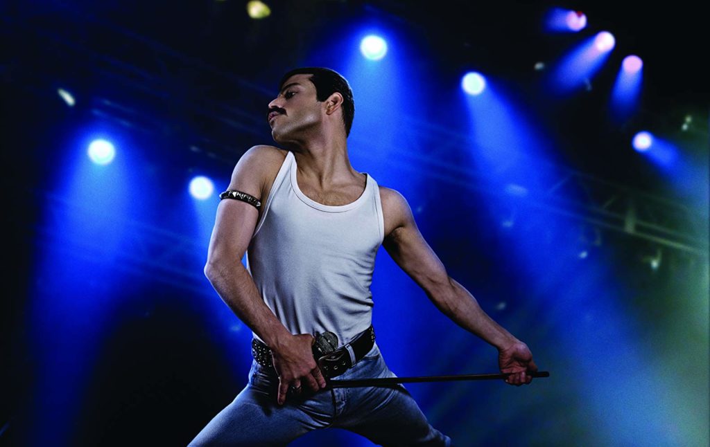 Freddie (Rami Malek) no palco, sensualizando com o suporte do microfone