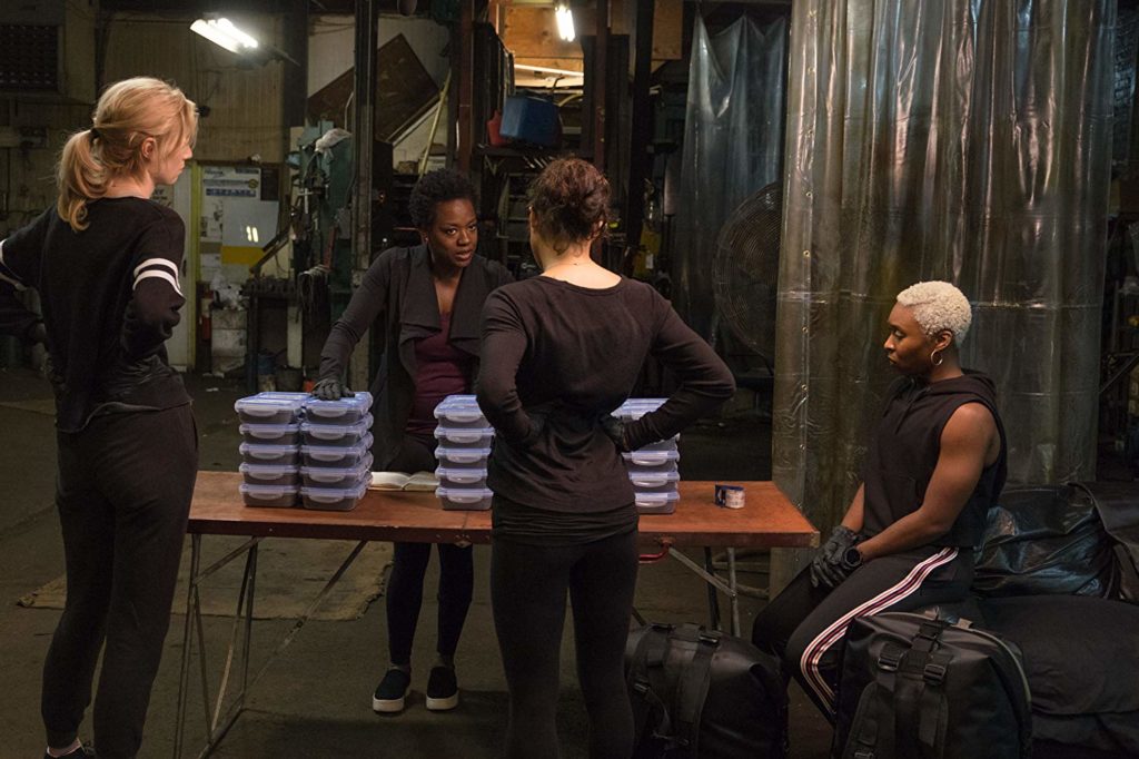 Viola Davis, Michelle Rodriguez, Elizabeth Debicki, Cynthia Erivo num galpão, ao redor de uma mesa, discutindo o plano