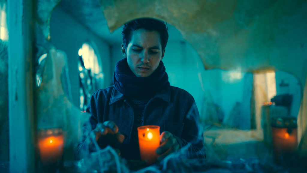 Theo acendendo velas, visto por uma janela quebrada
