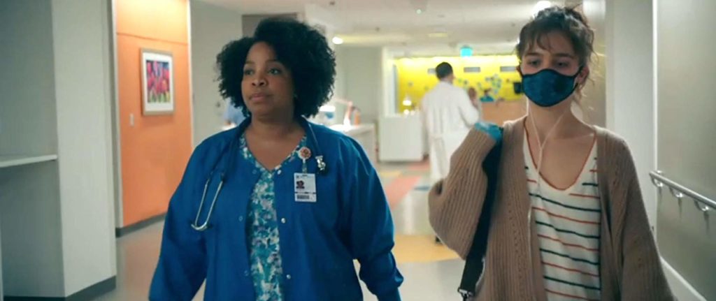 Stella andando ao lado de Barb (Kimberly Hebert Gregory), a enfermeira, que está conduzindo ela por um corredor do hospital