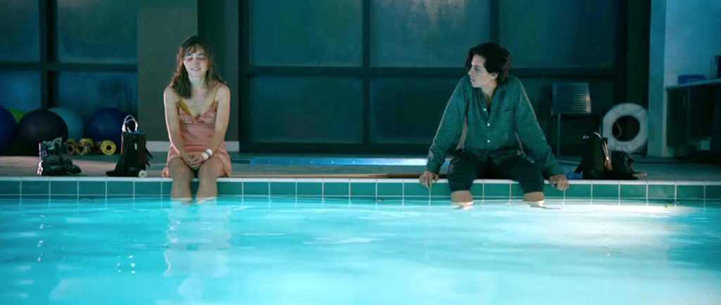 Stella e Will sentados na beira da piscina, com os pés na água. Ambos distantes como o título do filme sugere