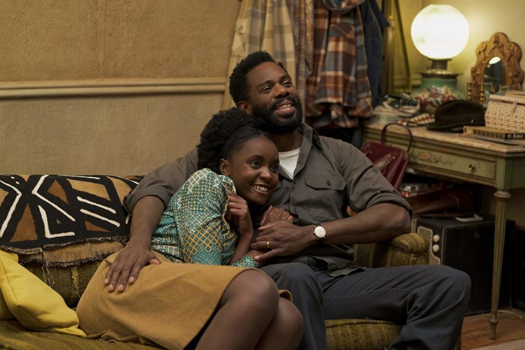 Tish, no sofá, sendo abraçada pelo pai (Colman Domingo), ambos sorridentes