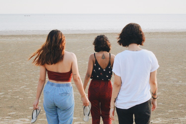 Três amigas caminham em direção ao mar. Maratona de Sofá.
