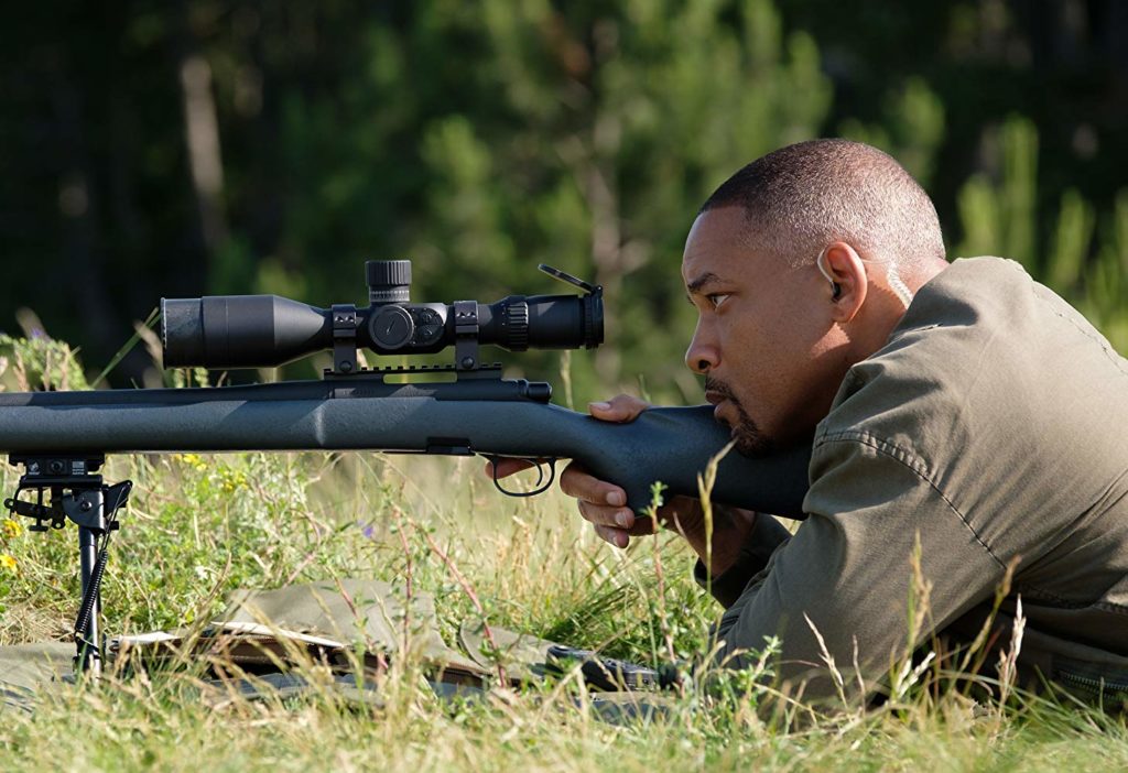 Henry (Will Smith) agachado no gramado, olhando através da luneta de um fuzil de longa distância (sniper)