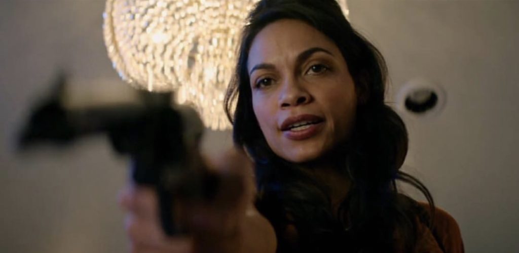 Nevada (Rosario Dawson) em close, câmera de baixo, apontando a arma para alguém ao lado da câmera.