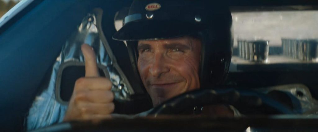 Ken Miles, de dentro do carro faz um sinal de positivo com o polegar para alguém do lado de fora.