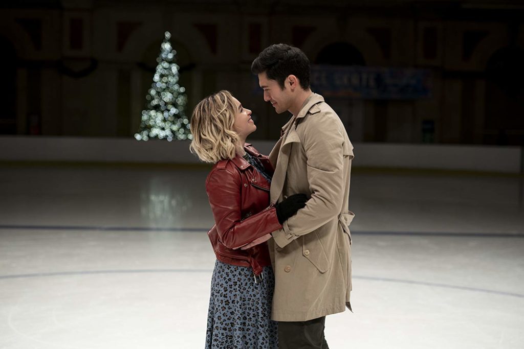 Tom e Kate estão abraçados numa pista de patinação no gelo. Ela, de saia e casaco vermelho. Ele, de casaco caqui. Ao fundo, pode ser vista uma árvore de natal desfocada