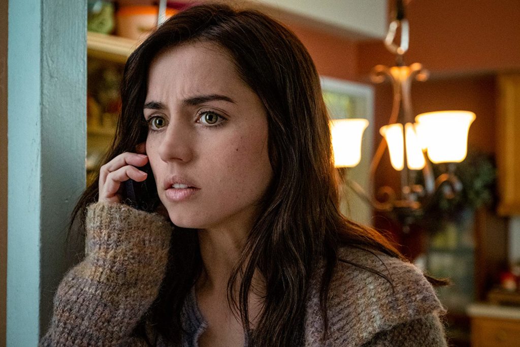 Em close, Marta (Ana de Armas) está apoiada no beiral de uma janela, falando ao telefone. Ao fundo, um dos quartos da mansão, onde se vê um lustre.