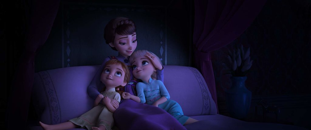 Numa cama, Elsa e Anna ainda crianças se aconchegam no colo da mãe