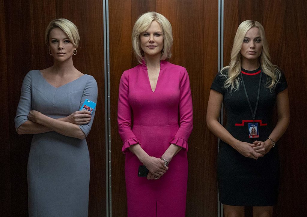 Dentro de um elevador com paredes de madeira, enfileiradas, estão Magyn, Gretchen e Kayla. As duas primeiras parecem muito seguras de si, ao contrário da Kayla