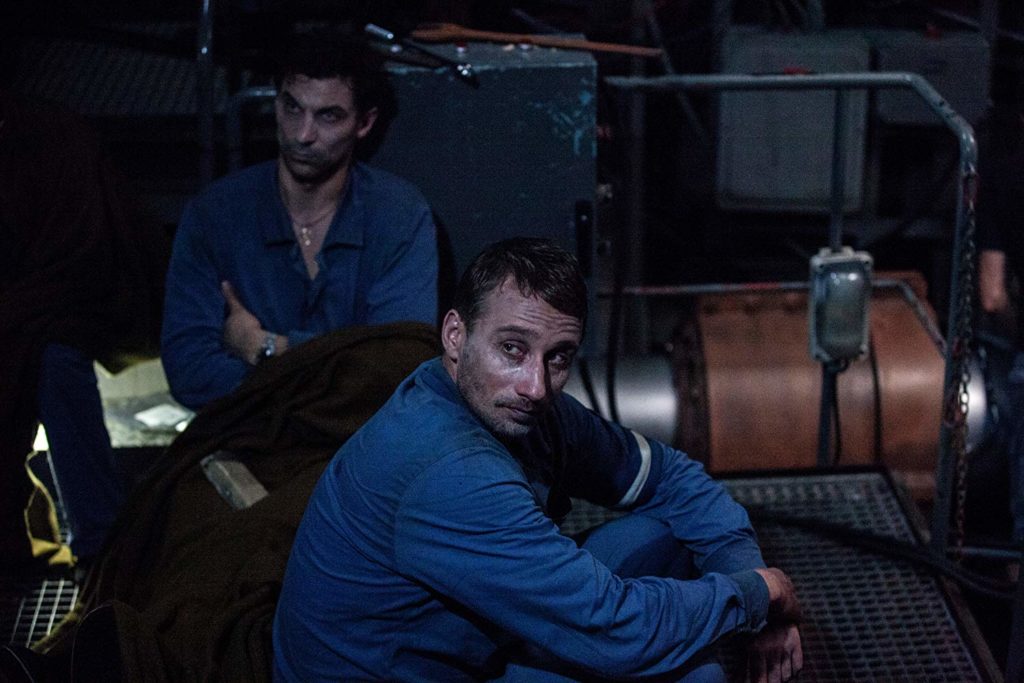 Mikhail (Matthias Schoenaerts) e mais um tripulante, sentado no piso metálico do submarino, com expressões miseráveis, esperando um possível resgate