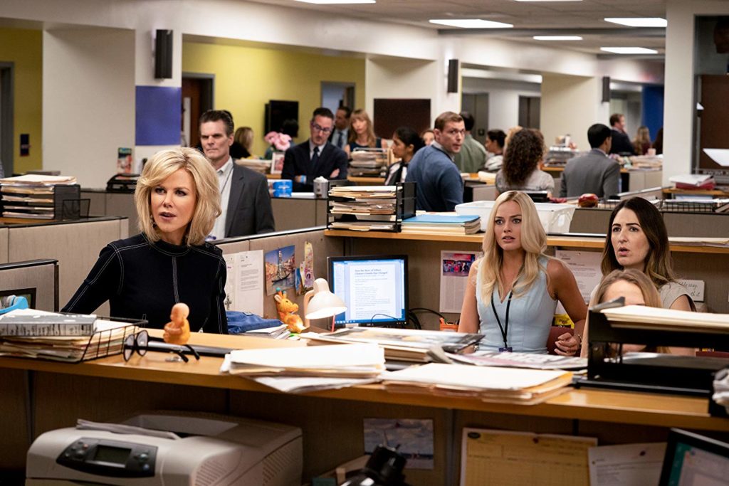 Mostrando a baia da sala de produção de dentro da fox, vemos Gretchen, Kayla, e Rebekah (D'Arcy Carden) olhando, incrédulas, para fora da baia. ao fundo, vemos vários profissionais, em suas baias, em pé, conversando, com diversos papeis espalhados.