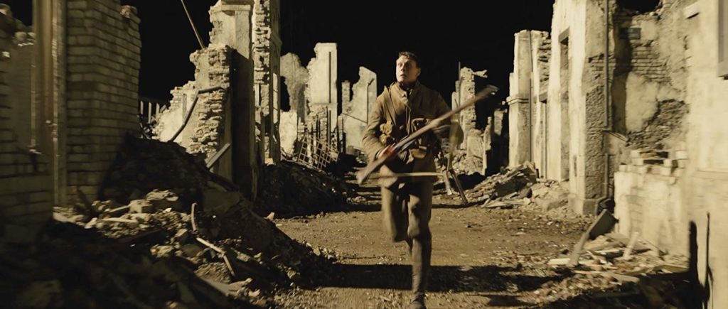 Em 1917, Schofield, rifle em punho, corre, entre ruínas de uma cidade. O ambiente está artificialmente iluminado, com luz muito forte, e sombras bem sólidas.