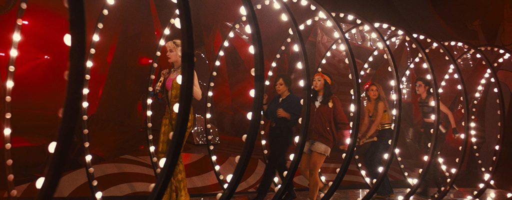Harley, Renee, Cassandra Cain (Ella Jay Basco), Canário (Jurnee Smollett-Bell) e a Caçadora (Mary Elizabeth Winstead) estão andando num tunel composto por anéis de metal com luzes incandescentes. É um brinquedo de parque de diversões antigo. O local está escuro, com iluminação avermelhada além das lâmpadas do túnel