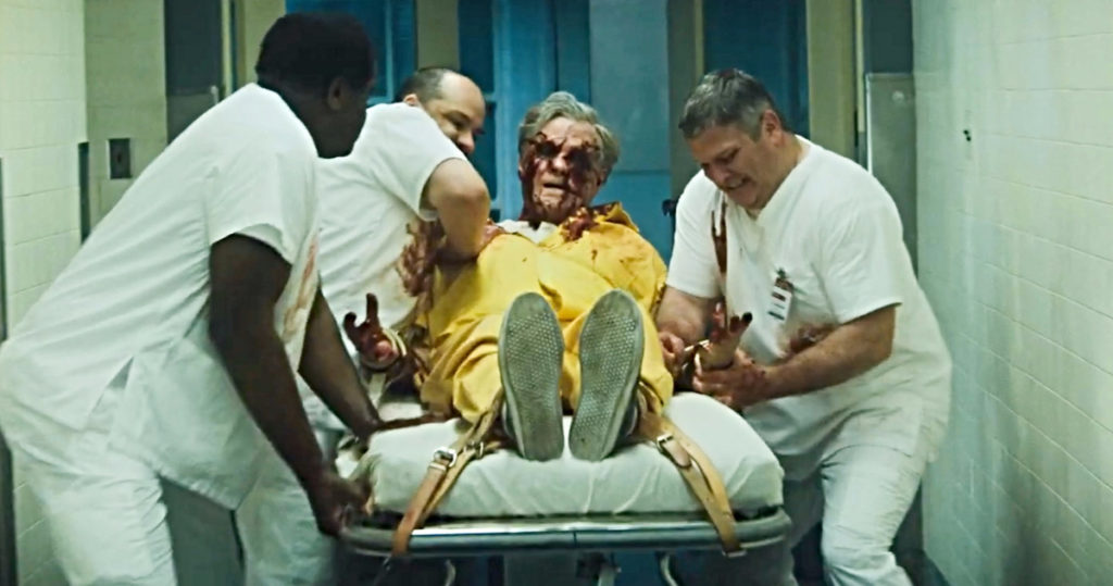 Três enfermeiros lutam para conduzir uma maca para fora de uma sala hospitalar. Sobre ela, o Detetive Wilson (William Sadler) está amarrado, se debatendo, e com os olhos furados, sangrando.