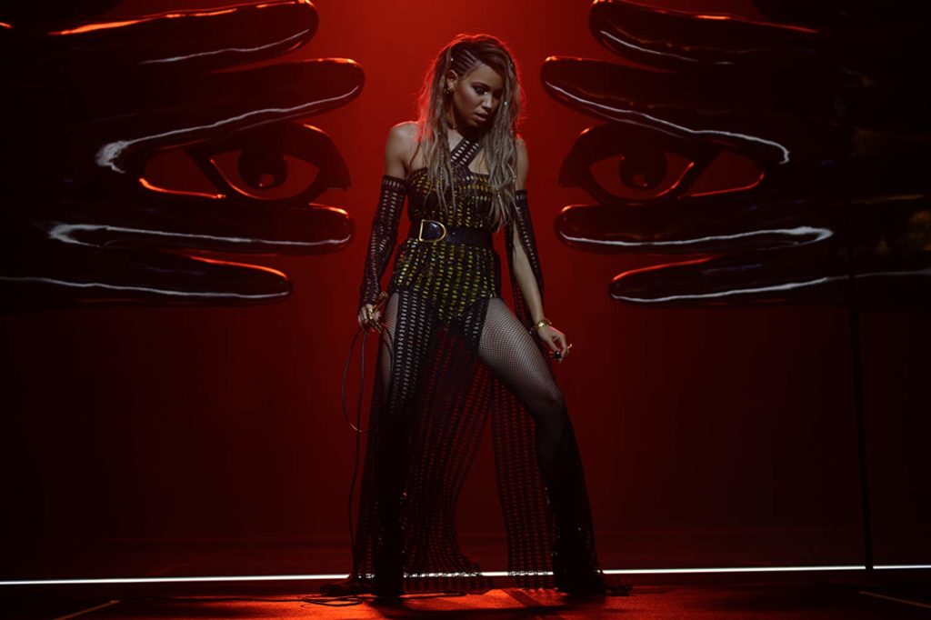 No palco, entre duas estátuas de mãos gigantes (que possuem representações de olhos entre os dedos médio e anelar), está a Canário Negro (Jurnee Smollett-Bell) no palco. Está usando um longo preto, com um microfone na mão direita, olhando para baixo, enquanto se prepara para cantar.