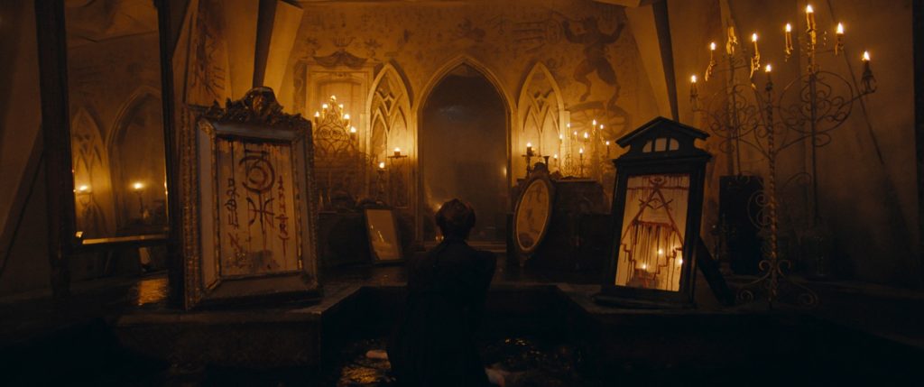 visão da alcova onde os rituais malditos eram realizados, com diversas velas, pinturas e inscrições.
