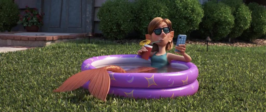 visão de um jardim gramado de uma casa. Uma sereia está dentro de uma piscina de plástico, tomando um drinque num copo de plástico, e olhando o celular, enquanto usa oculos escuros.