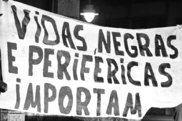 Imagem em preto e branco. Cartaz escrito "VIDAS NEGRAS E PERIFÉRICAS IMPORTAM"