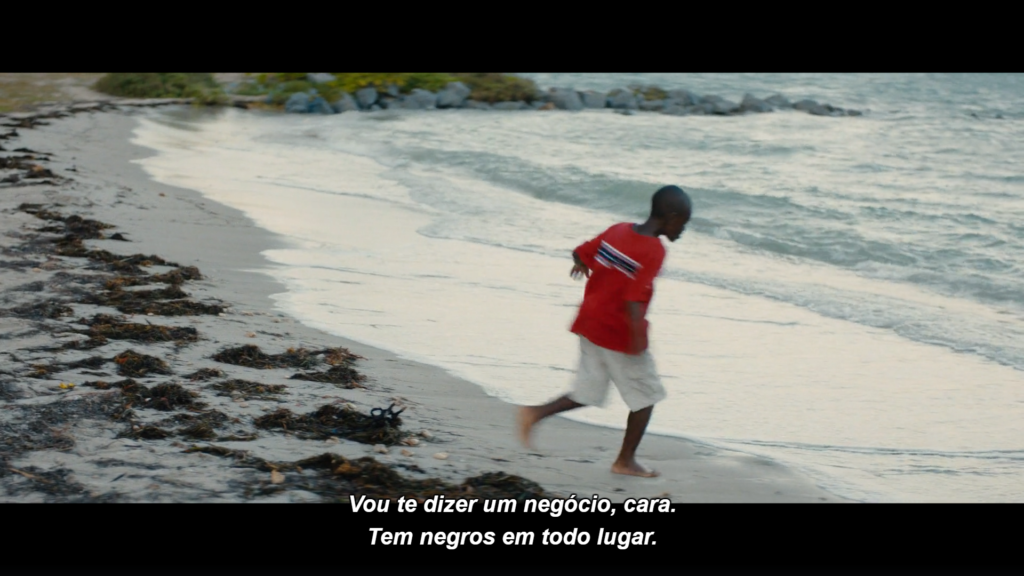 Cena do filme Moonlight: Chiron, vestido com uma bermuda bege e uma camiseta vermelha, corre na praia, se esquivando as ondas que quebram na areia. Na legenda, lemos "Vou te dizer um negócio, cara.  Tem negros em todo lugar"