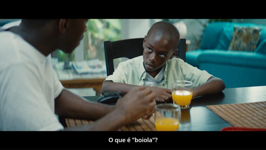 Cena de Moonlight. Sentados ao redor de uma mesa de madeira, com copos  de suco postos, Juan e Chiron se encaram. Chiron pergunta "O que é 'boiola'?", com olhar muito sério.