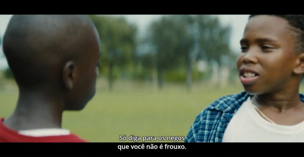 Cena de Moonlight. Kevin e Chiron estão em uma área gramada. Estão em close, fechado, onde podemos vê-los afastados um do outro por meio metro. Kevin está falando para Chiron, "Só diga pra os negos que você não é frouxo"