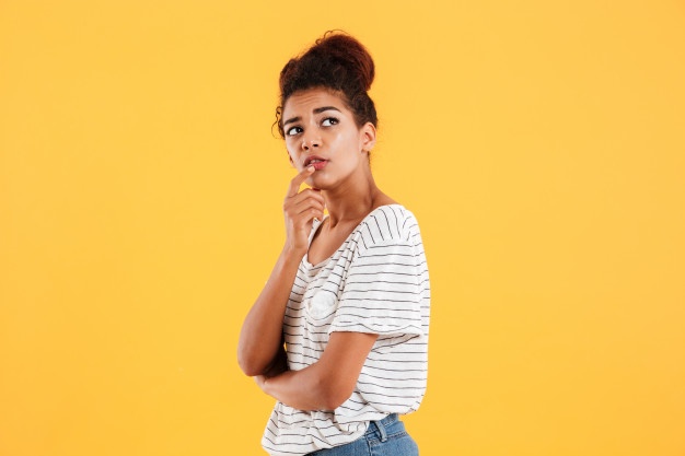 Mulher negra, de camiseta branca, sob um fundo amarelo, refletindo.