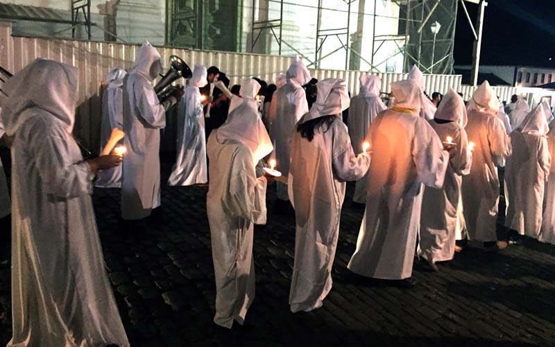 Pessoas vestidas de branco, com velas na mão caminham durante a procissão das almas.