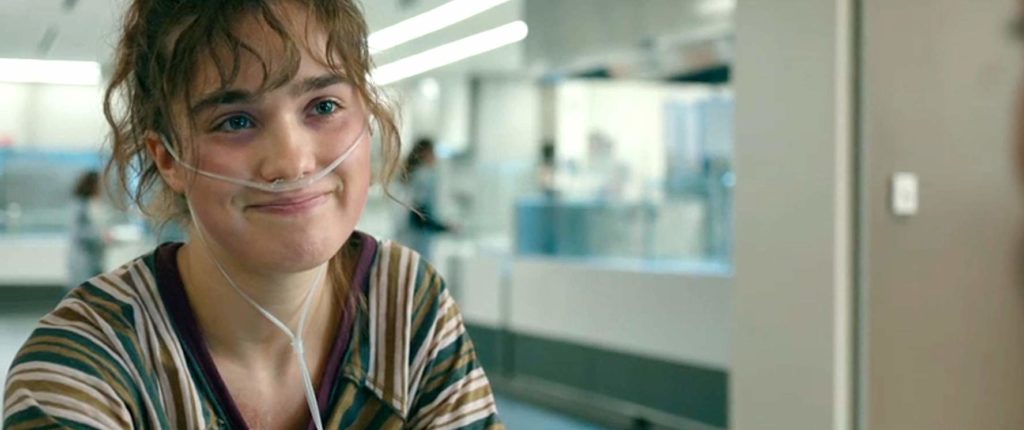 Stella com tubos no nariz, dentro de uma sala de hospital, sorrindo