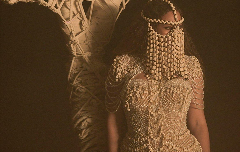 Beyoncé utiliza um ornamento feito com conchas - ou búzios - que cobre todo seu rosto, exceto olhos, casando com um vestido também com diversas conchas.