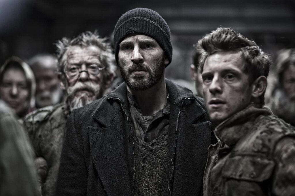 Cena do filme Snowpiercer de 2013. Ao centro, Curtis (Chris Evans), rodado por diversas outras pessoas, estão com olhar apreensivo olhando para frente. Estão todos com casacos contra o frio