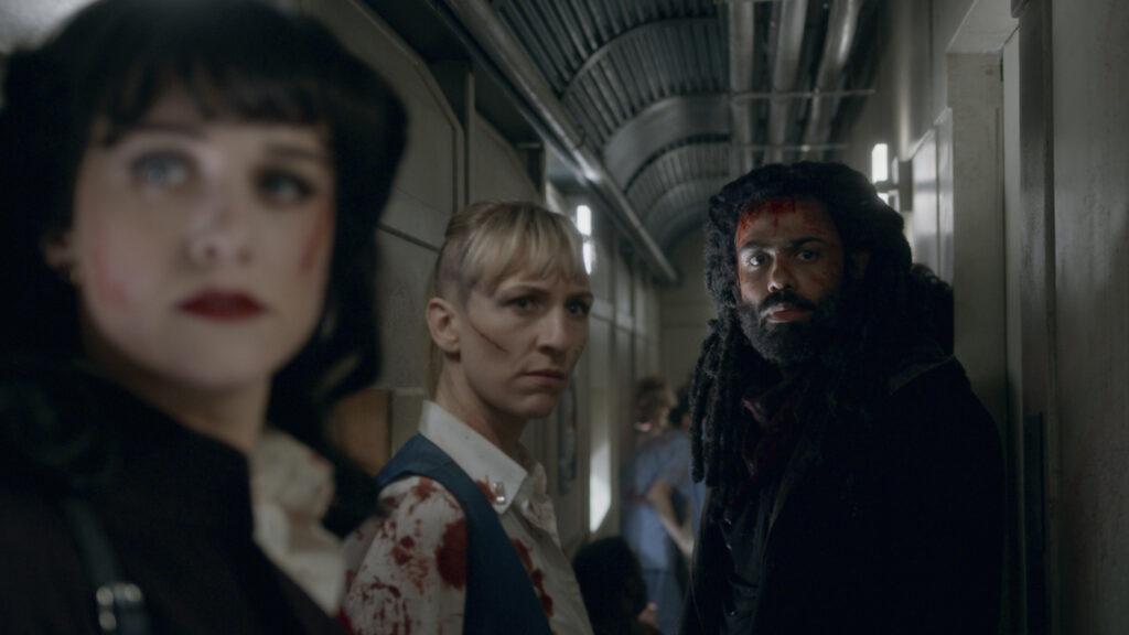 Em primeiro plano (Desfocada) Audrey olha para trás, sendo acompanhada por Till e Andre. Estão num dos corredores do Snowpiercer