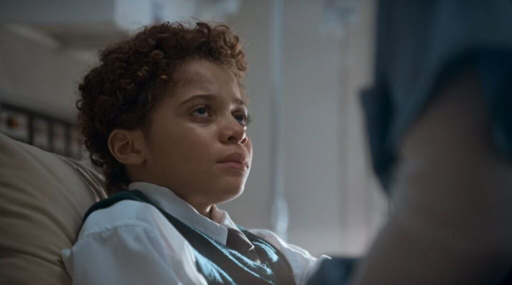 Deitado numa maca, Miles olha , com aspecto cansado, para uma enfermeira (vemos apenas o seu braço)