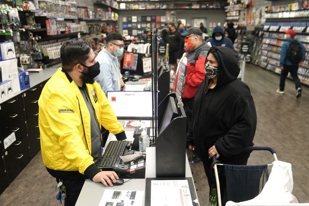 Foto do interior da Gamestop.  Paredes cobertas por prateleiras cheias de jogos, e clientes interagindo com os vendedores.