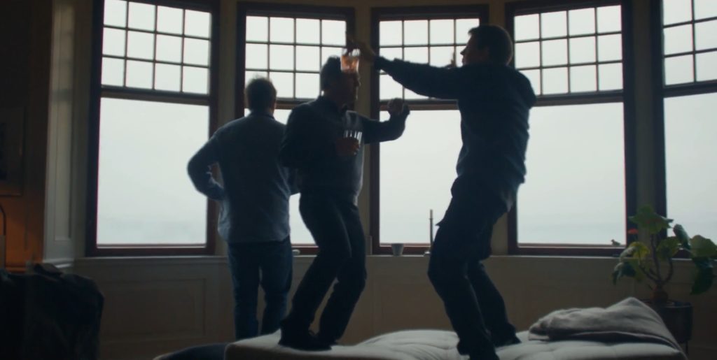 3 personagens do filme bebem e dançam em cima de um sofá numa casa