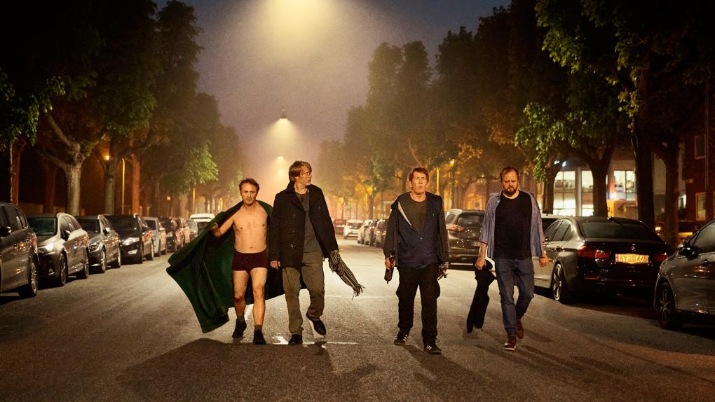 Os quatro protagonistas andam juntos na rua a noite, um deles de cueca e roupão aberto, e todos maltrapilhos.