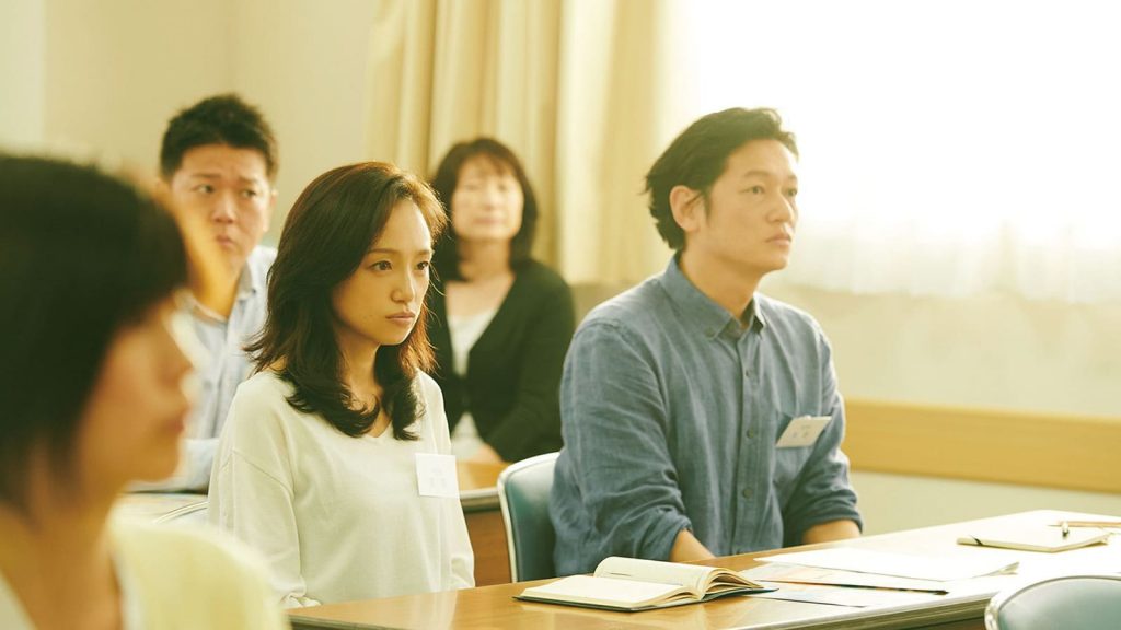 Imagem de Mães de Verdade. O casal Satoko e Kiyokazu está sentado, observando uma palestra