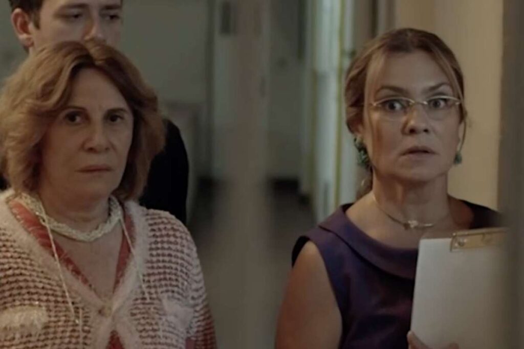 Cena de Medida Provisória. Em close, Adriana Esteves (Isabel) e Dona Izildinha (Renata Sorrah). Ao fundo, vemos Santiago (Pablo Sanábio). Eles estão num dos corredores do edifício onde vivem André e Antônio.
